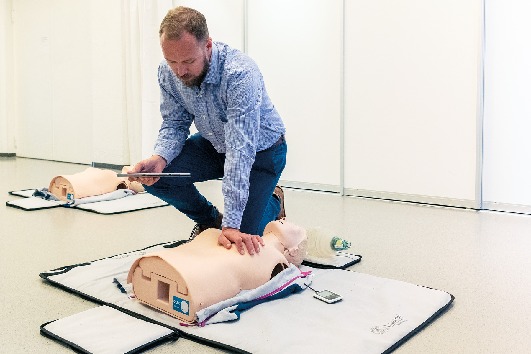 man in blue shirt training on manikin in a plain bright room