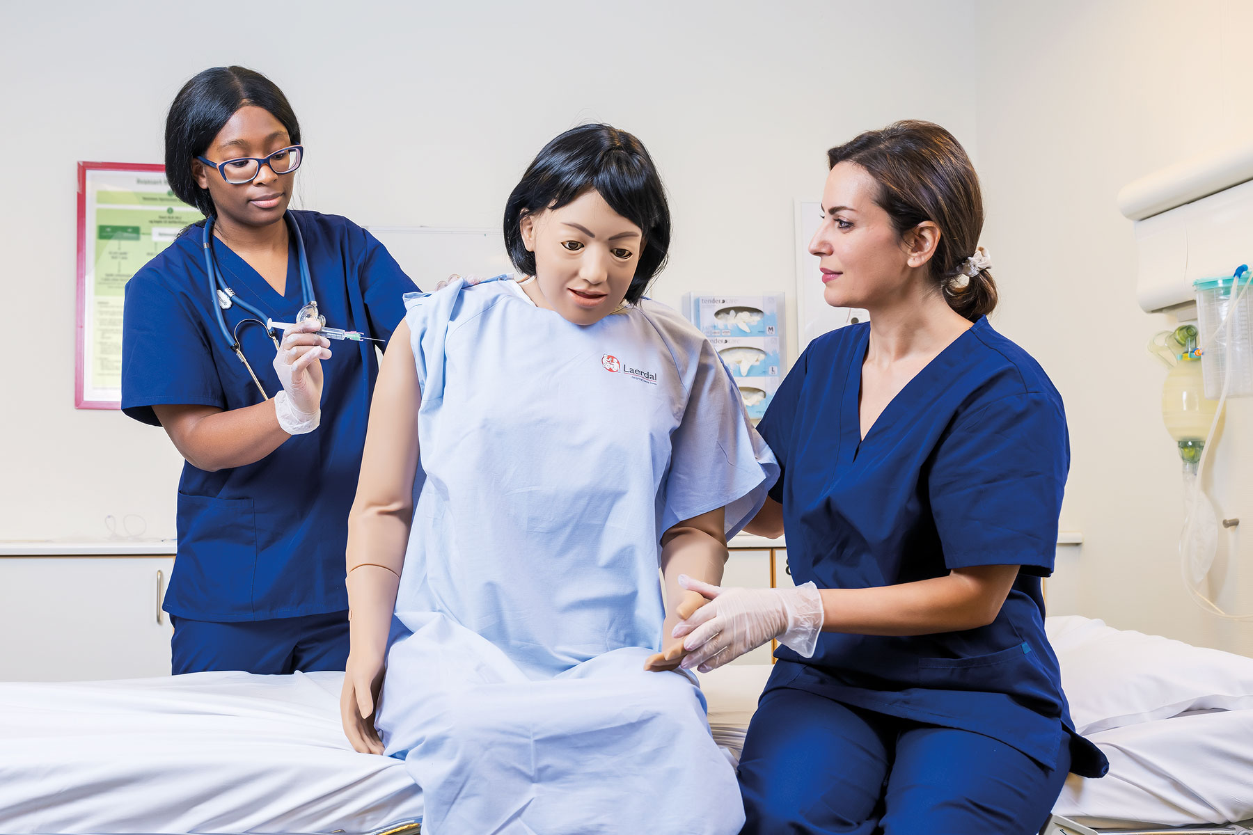 Dwie pielęgniarki opiekujące się Nursing Anne Simulator, jedna robi zastrzyk