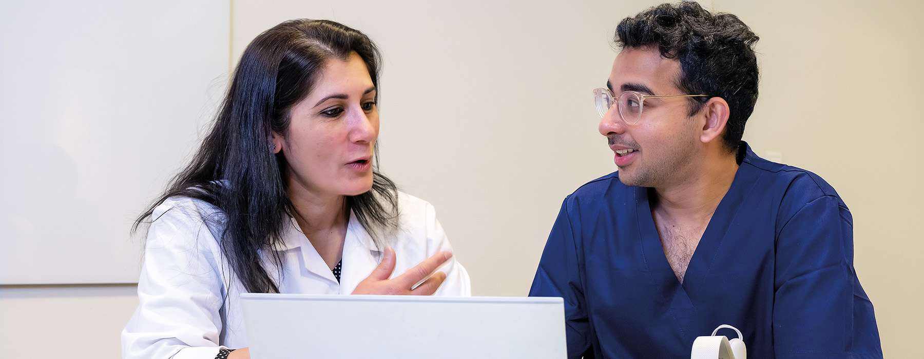 A clinical instructor provides guidance and feedback to a healthcare student during a collaborative debriefing session with a laptop.