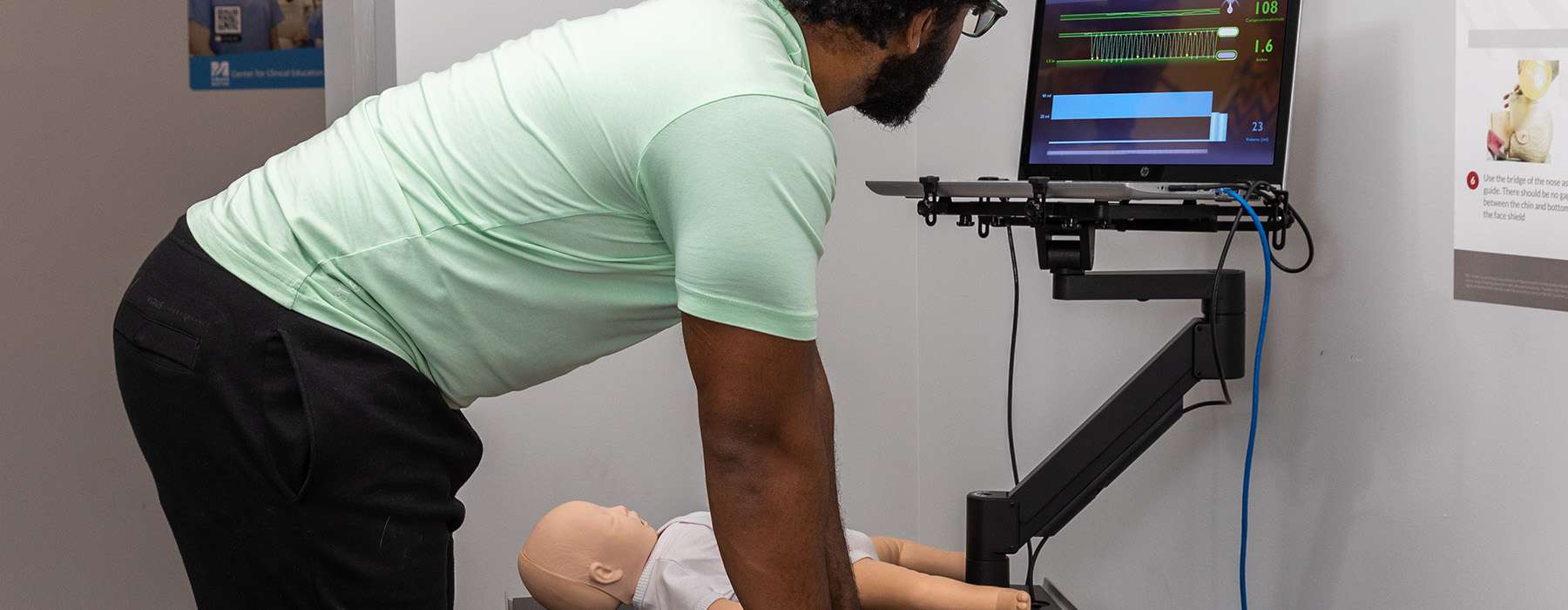 A student performing CPR on a simulator while monitoring compression depth and rate on a digital training screen.
