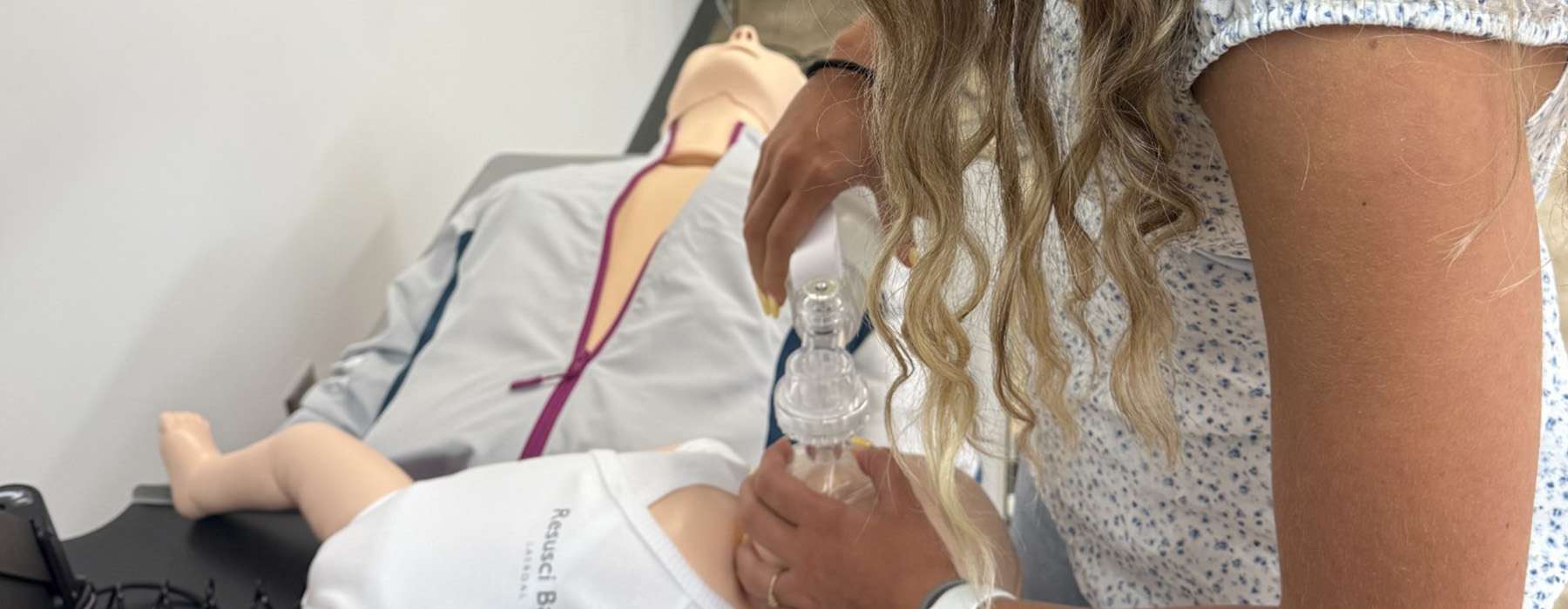 A healthcare student practicing bag-mask ventilation on an infant simulator in a modern clinical training environment.