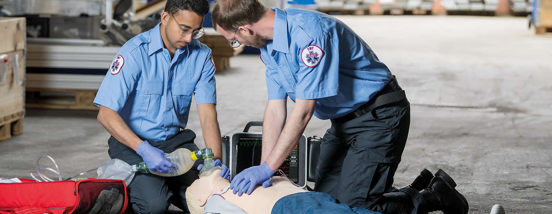 Two first responders practicing CPR and ventilation on a patient simulator while using a clinical monitor to track vitals.