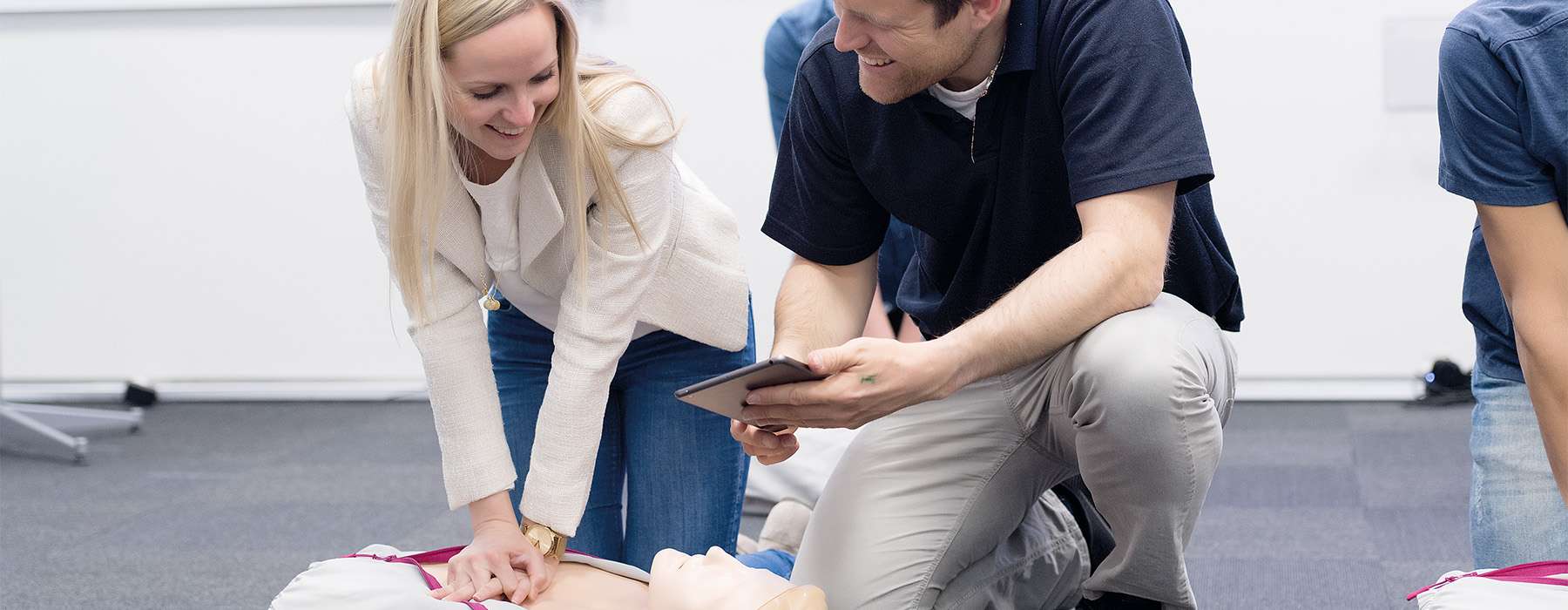 Two individuals reviewing performance data on a tablet while one practices chest compressions on a medical mannequin.