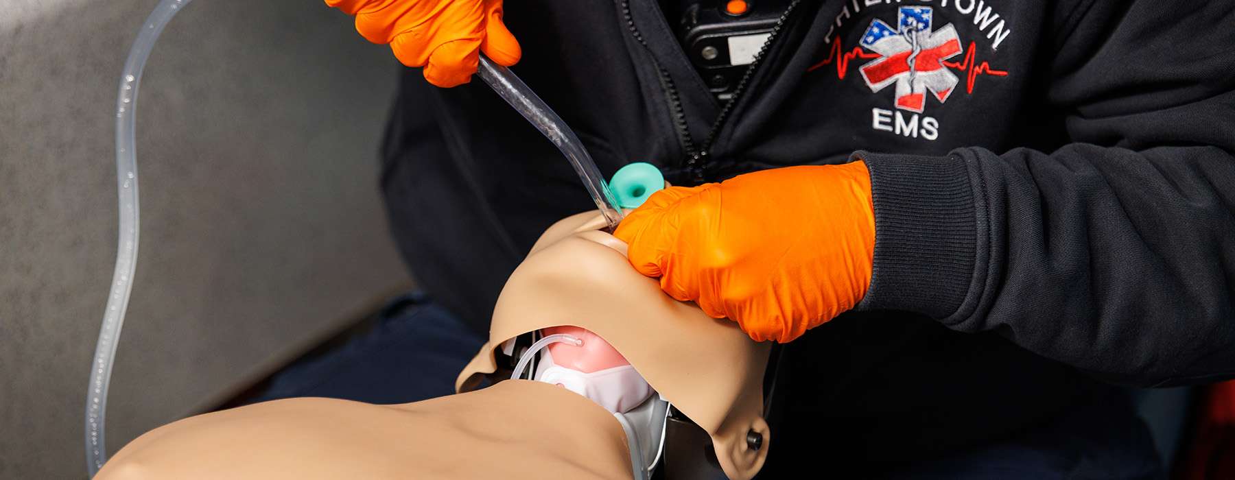 A close-up of a healthcare provider in orange gloves practicing airway management skills on a patient simulator