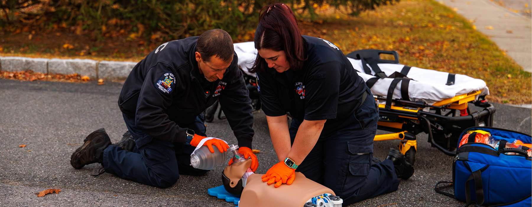 A team of two EMS professionals practicing outdoor resuscitation, including chest compressions and bag-valve-mask ventilation.