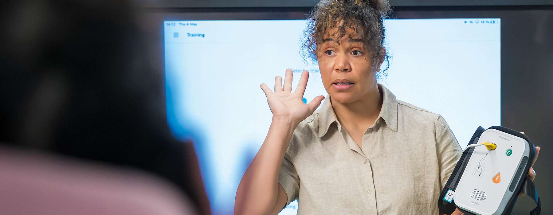 An instructor explains the features and operation of an AED trainer unit during a workshop.
