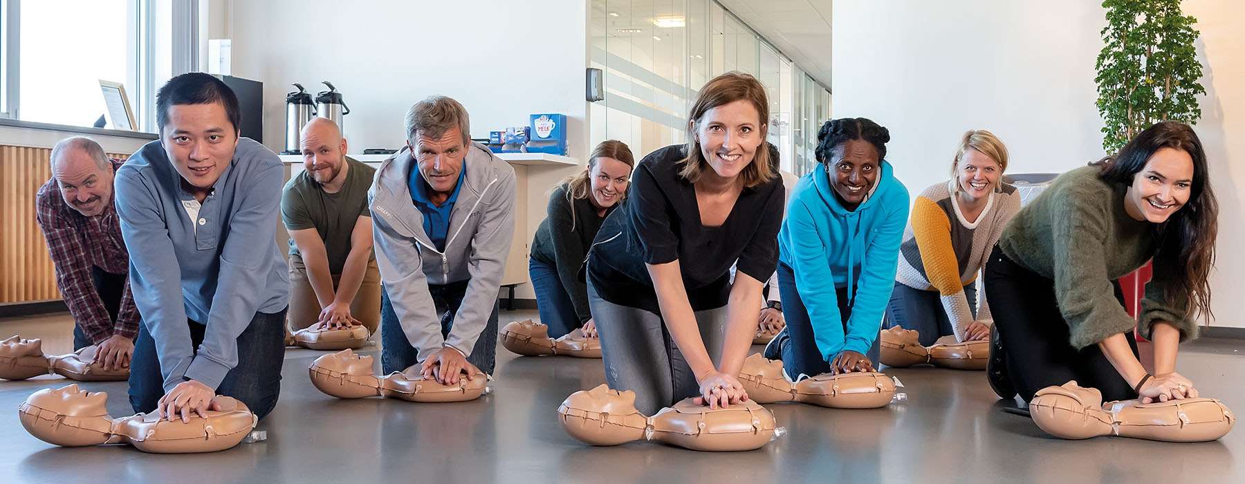 A large group of diverse participants practice chest compressions on portable manikins during a community-based life-saving skills class.