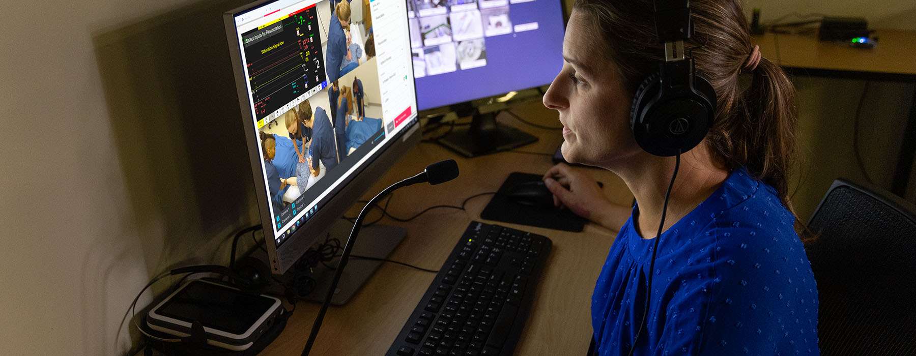 debriefing-control.jpg	A healthcare professional wearing a headset monitors and controls a remote simulation session via a multi-screen digital interface.
