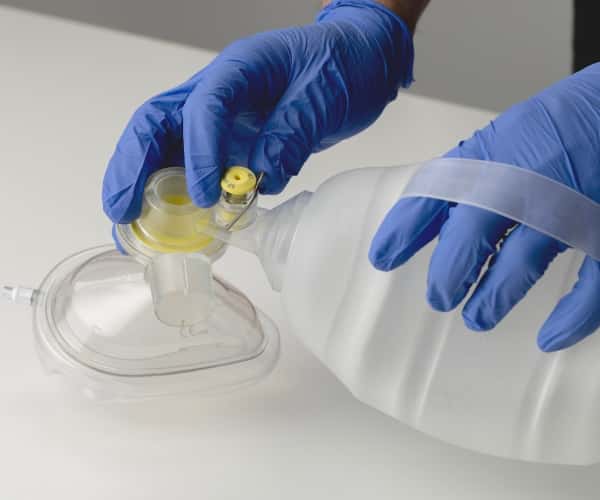 Gloved hands demonstrating use of manual resuscitator with oxygen mask 