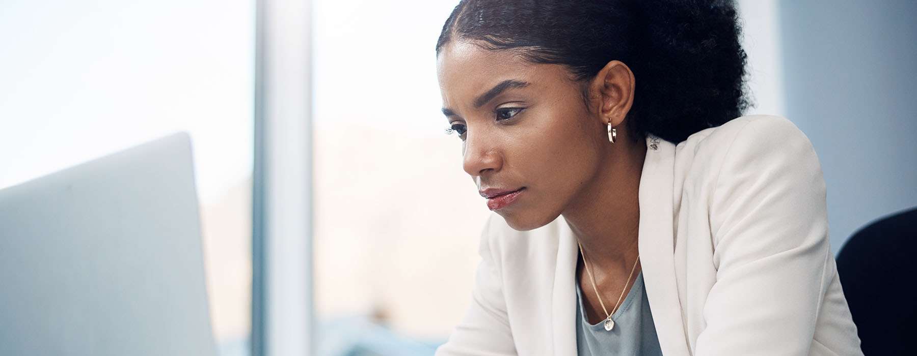 A closeup of a woman in a white lab coat looking at a computer screen