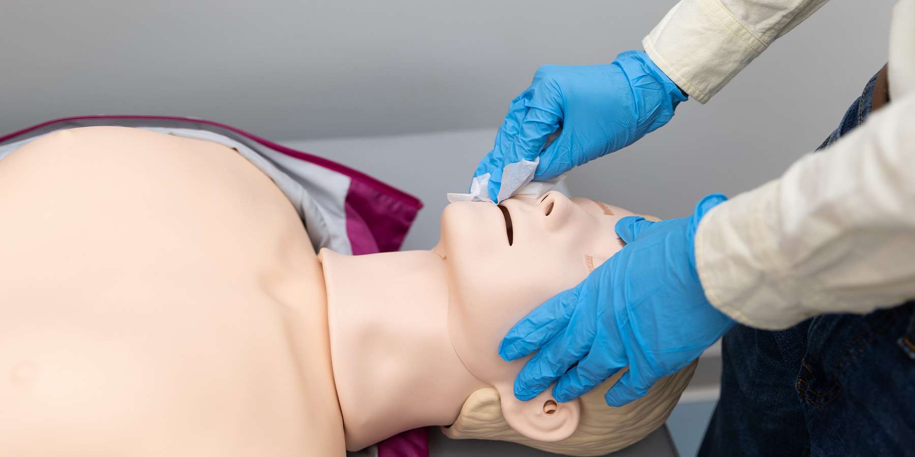 Person wearing gloves wiping a manikin. RQI cart. 