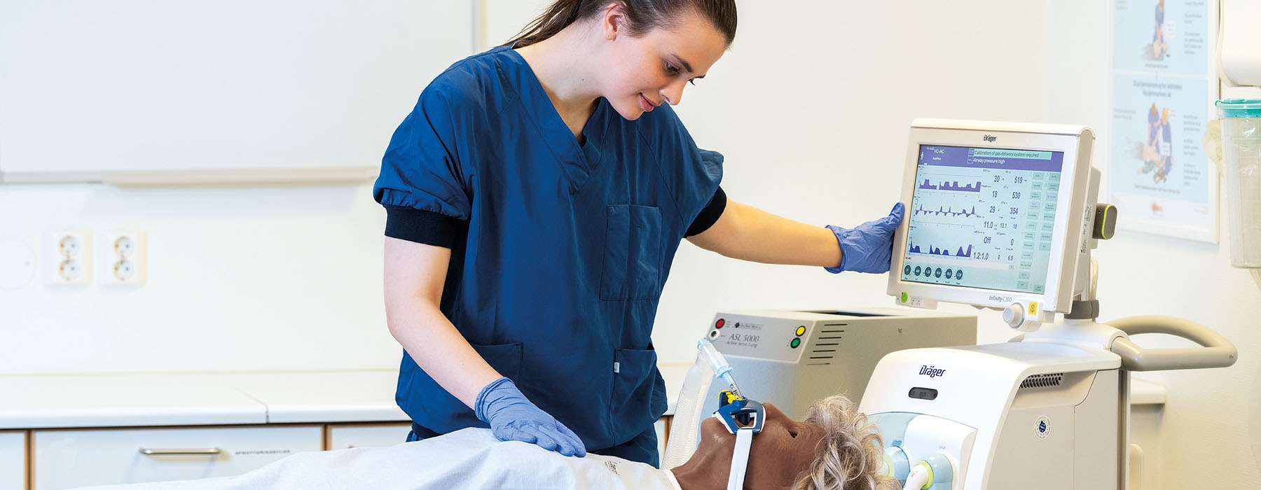 A nurse in blue practicing geriatric care on a geriatric manikin.