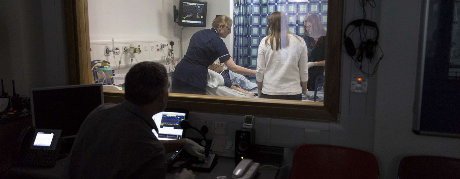 Man observing a team of healthcare workers doing simulation training in a separate room.