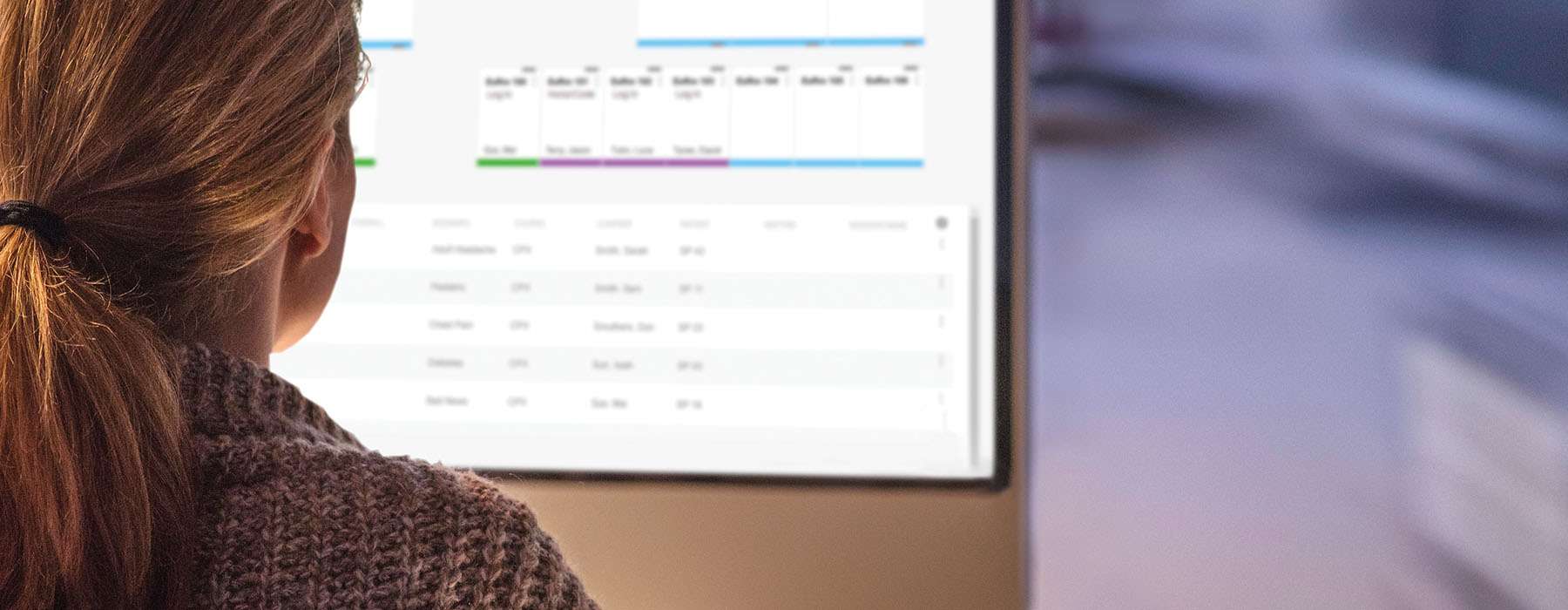 Close-up back view of a woman reviewing stats on a large computer screen