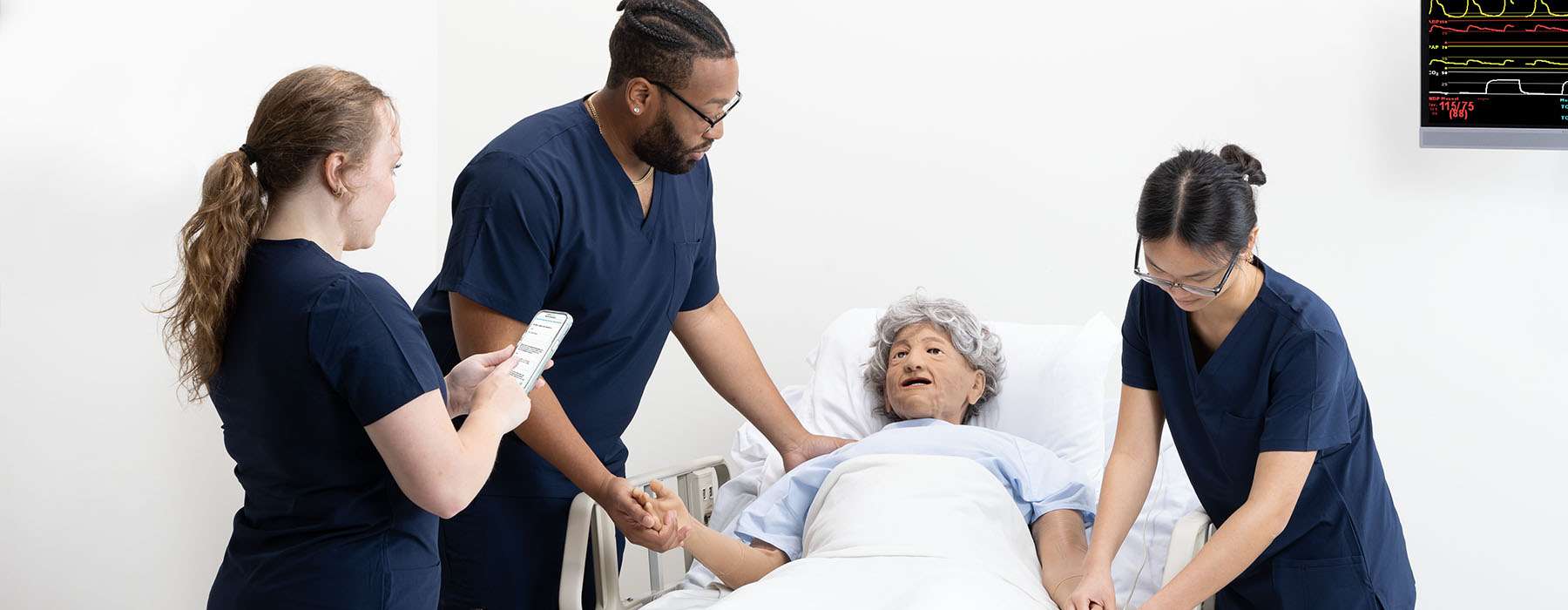 Three nurses in blue uniform performing simulation training on Nursing Anne Geriatric