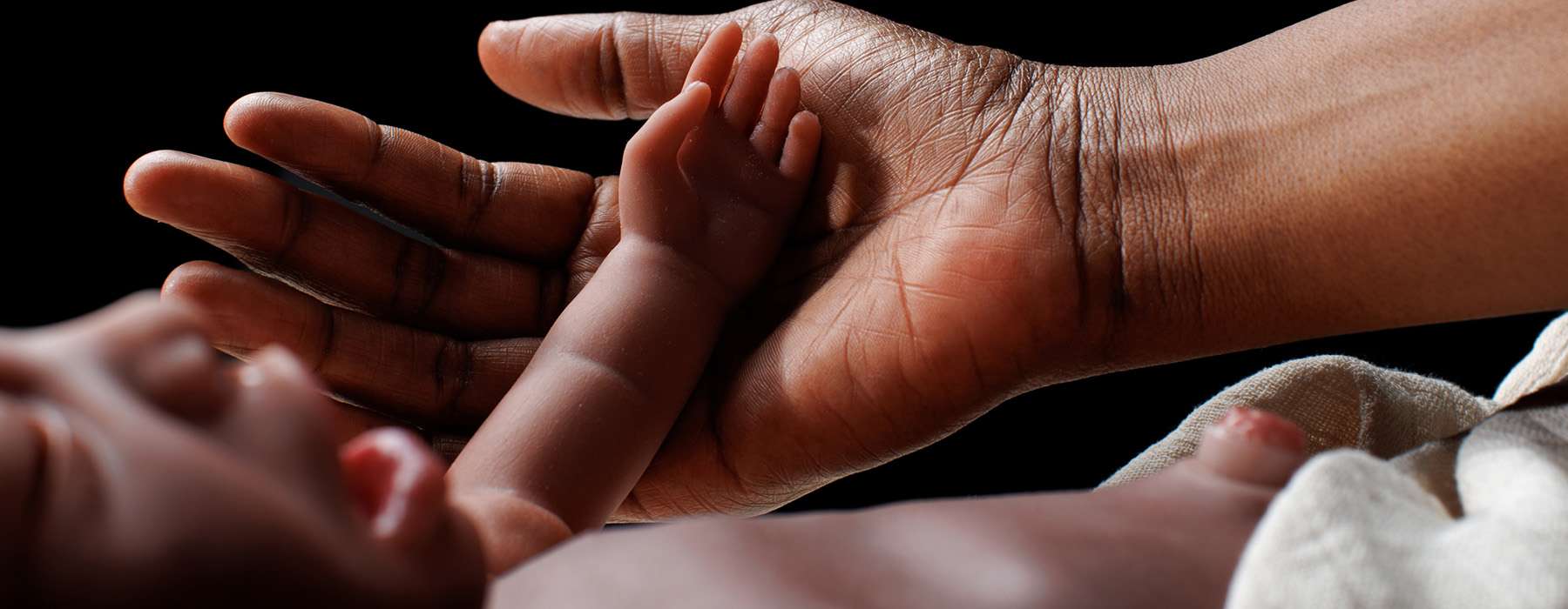 A close-up view of an adult's hand gently supporting the small arm and hand of a newborn baby.