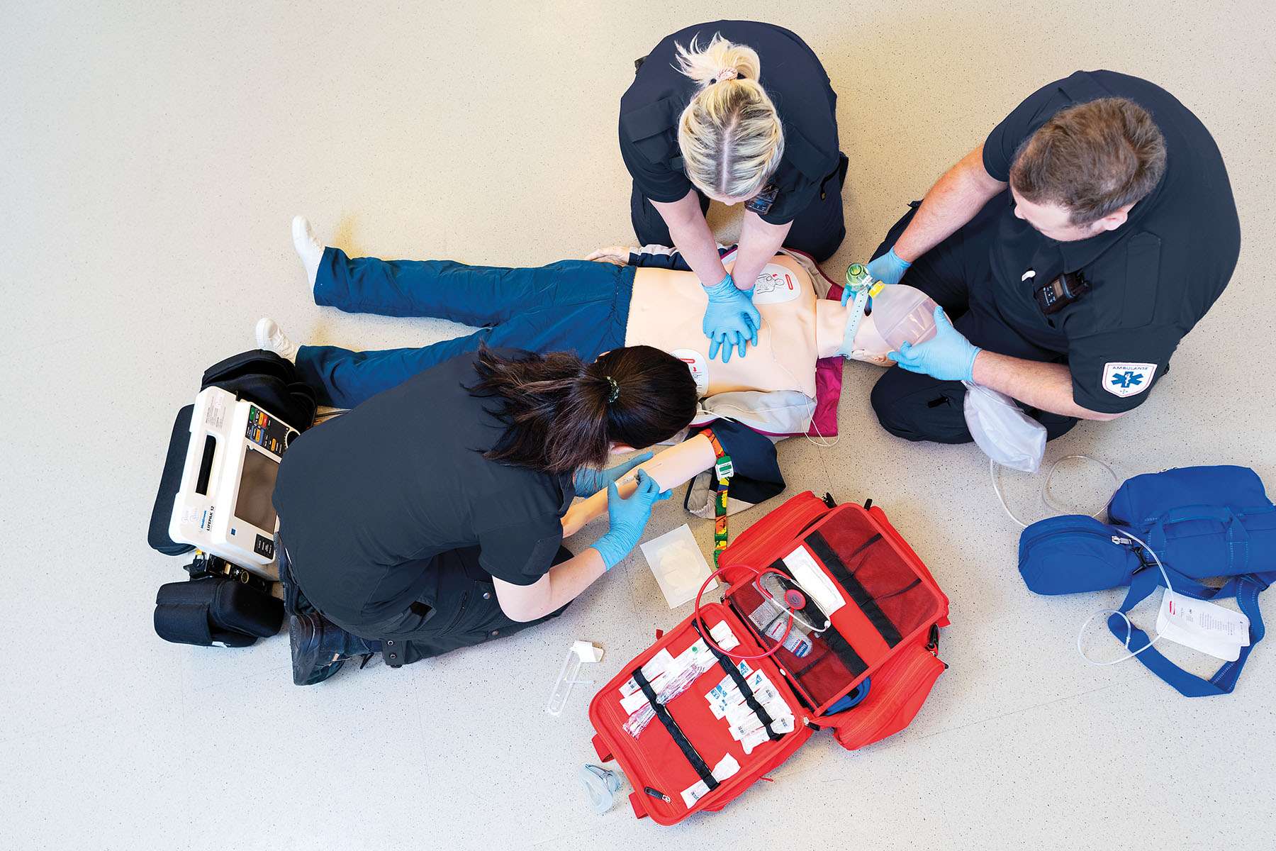A top-down view of three Emergency Medical Services (EMS) professionals performing CPR and emergency procedures on manikin during team training.