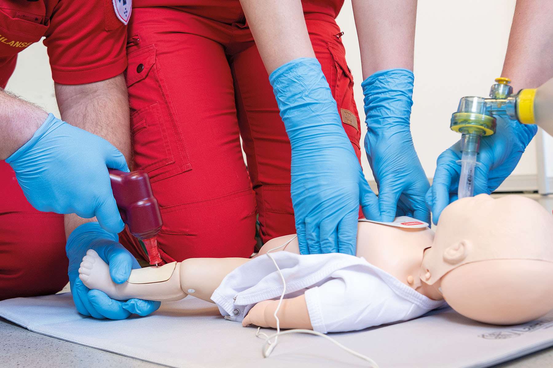 A close-up view of a medical team wearing blue gloves practicing CPR training on a baby patient simulator.