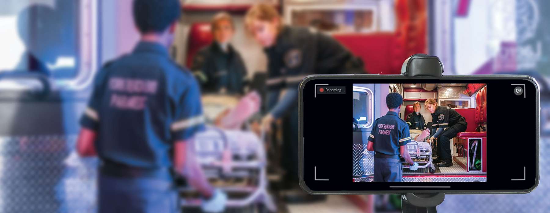 A mobile phone screen recording a team of paramedics moving a patient into an ambulance, highlighting the use of mobile applications for recording and debriefing simulation training.