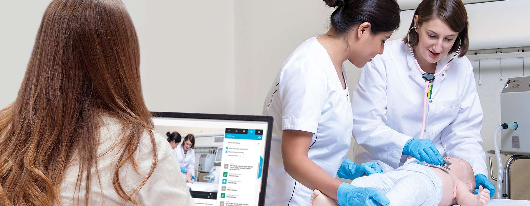 Healthcare providers practicing infant care on a simulator while the session is being recorded for debriefing on a nearby screen.