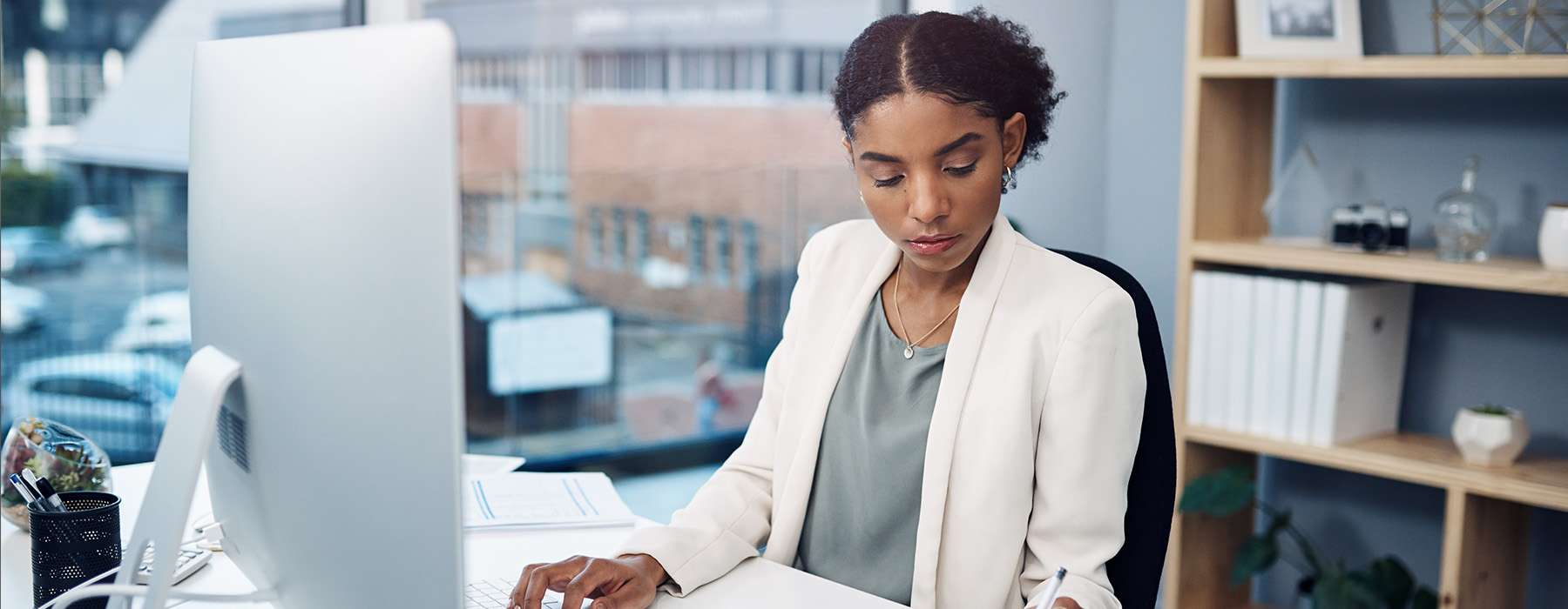 A professional woman working at a desk with a large computer monitor in a modern office or clinical setting.