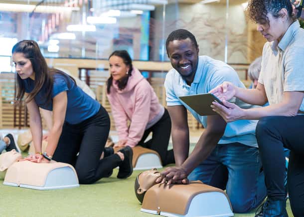 A group of individuals practicing CPR on several Little Anne torso training manikins