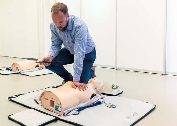 man in blue shirt training on manikin in a plain bright room